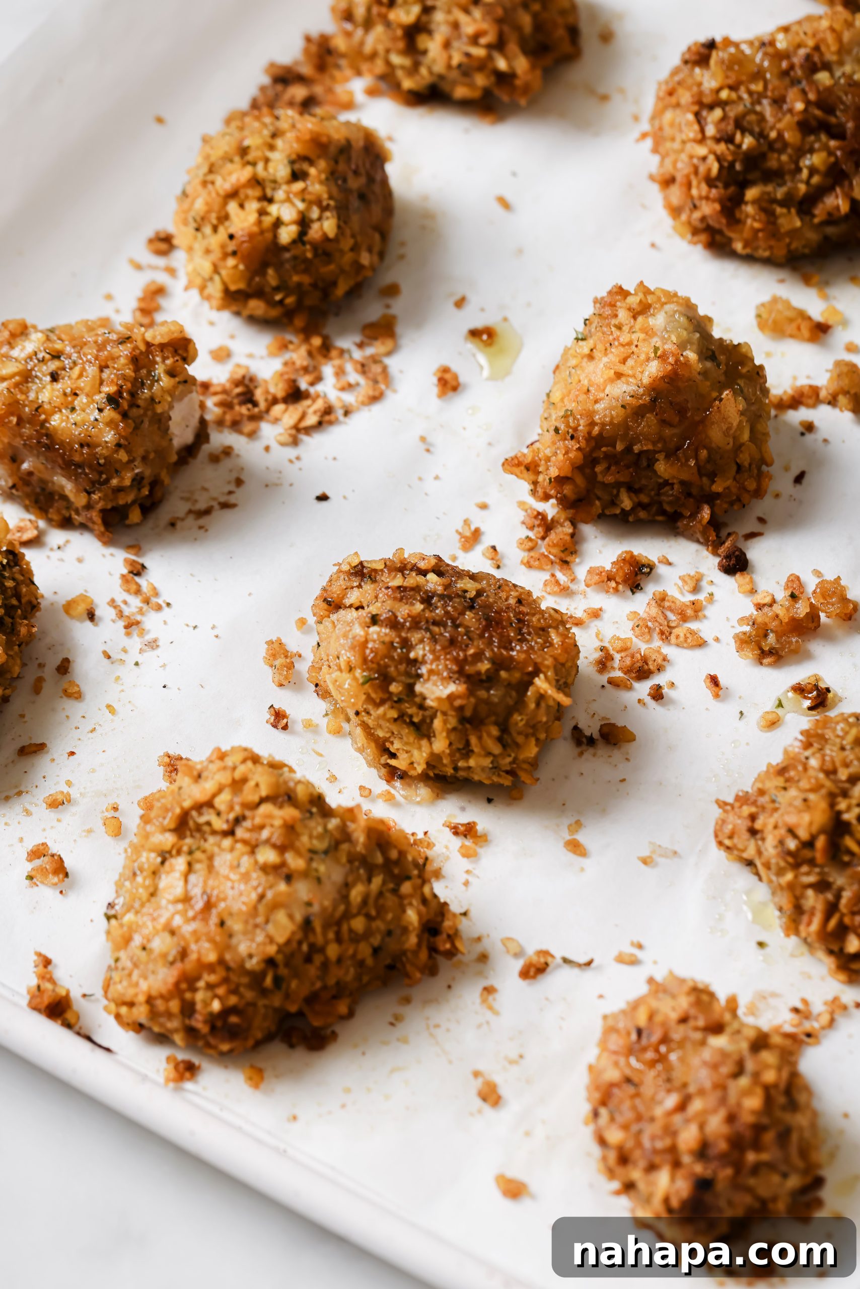 A close-up shot of baked crispy chicken nuggets on a parchment-lined baking sheet, golden and ready to eat.
