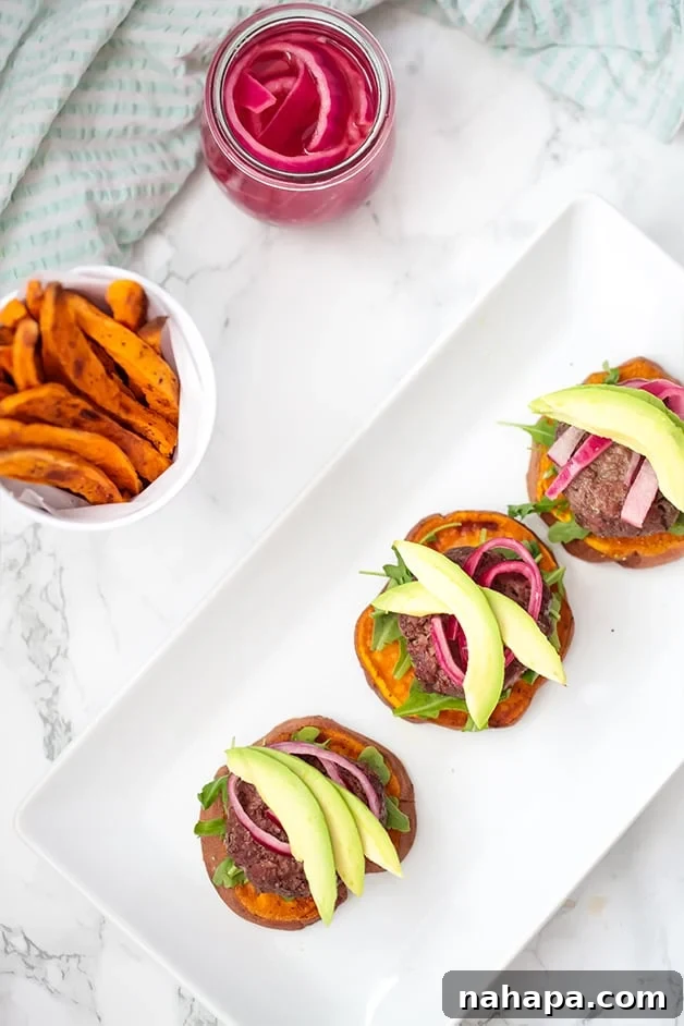 A white plate showcasing three sweet potato sliders alongside a bowl of sweet potato fries. The sliders are vibrant with fresh toppings.