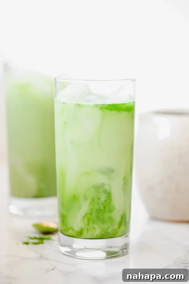 Two glasses filled with creamy, vibrant green iced matcha lattes, garnished with a sprinkle of matcha powder.