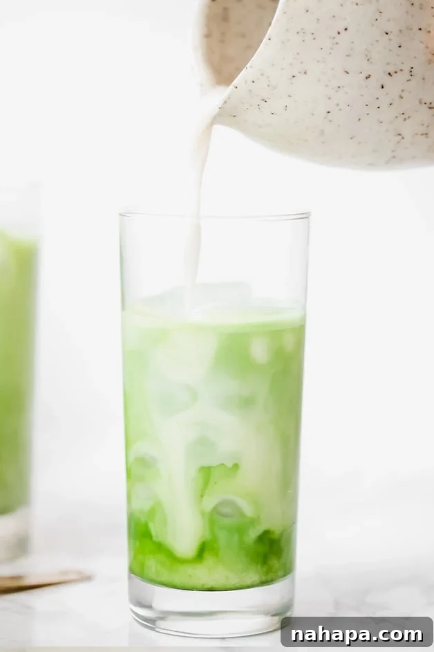 A single glass of iced matcha latte, topped with a delicate foam, showcasing its inviting green color.