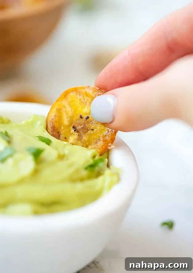 A close-up shot of baked plantain chips with a small bowl of guacamole, ready for dipping.
