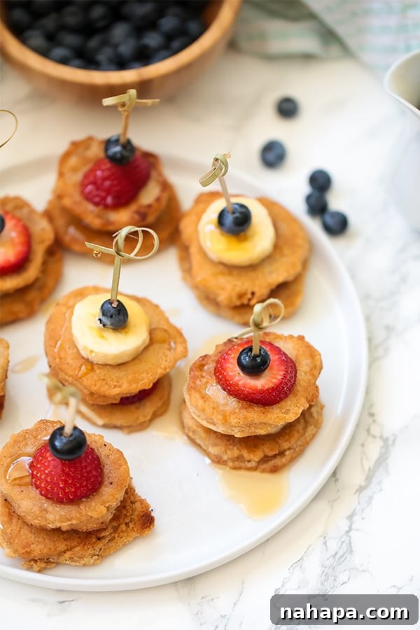 Delicious Paleo Vegan Gluten Free Pancake Skewers 5 A white plate with mini pancakes on skewers with fresh fruit.