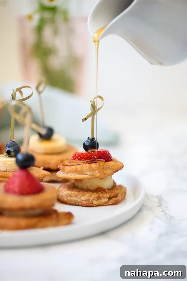 A white plate with mini pancakes on skewers with fresh fruit.