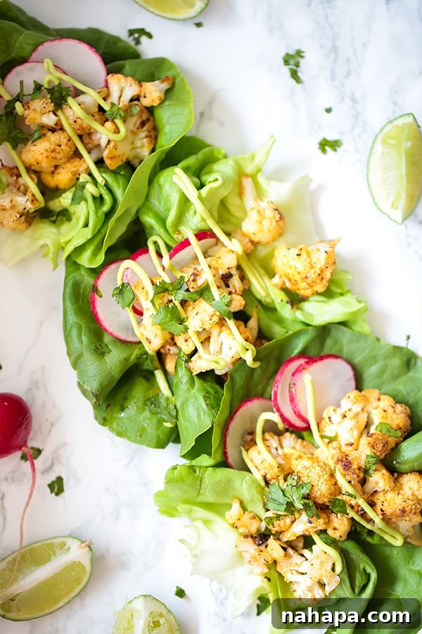 Three perfectly arranged Bang Bang Cauliflower Tacos, nestled in fresh lettuce cups, presented on a light-colored countertop. A vibrant lime wedge adds a pop of color and promises a fresh finish.