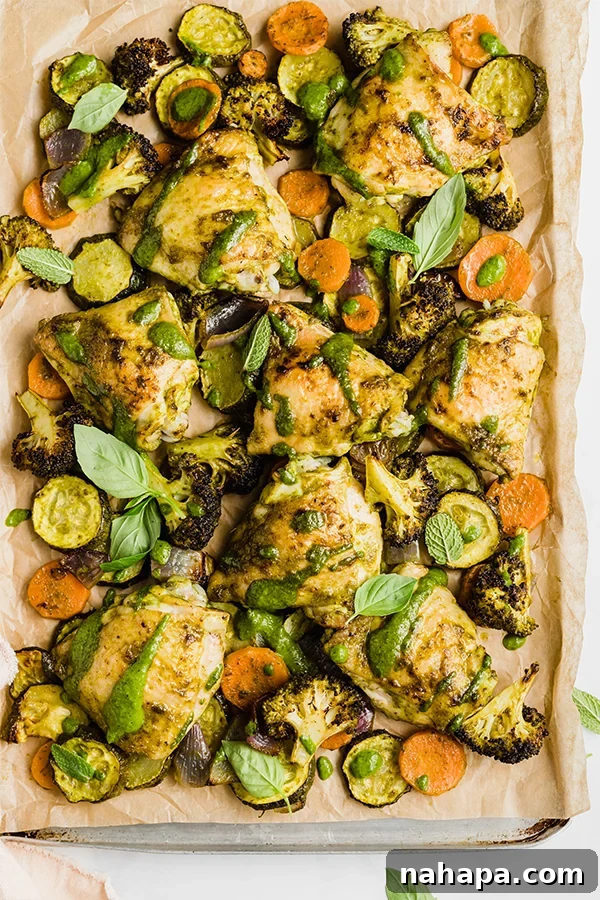 Overhead shot of one-pan chicken pesto and vegetables cooking on a baking sheet, showing golden chicken and vibrant roasted veggies.