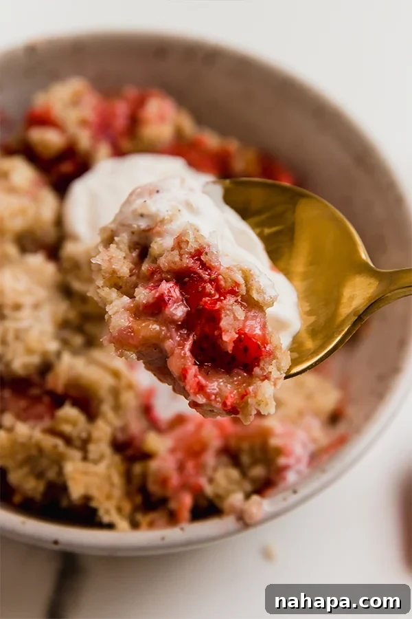 Paleo AIP Vegan Strawberry Rhubarb Crumble 7 A close-up of a spoonful of strawberry rhubarb crisp, highlighting the juicy fruit filling and the golden, crumbly topping.