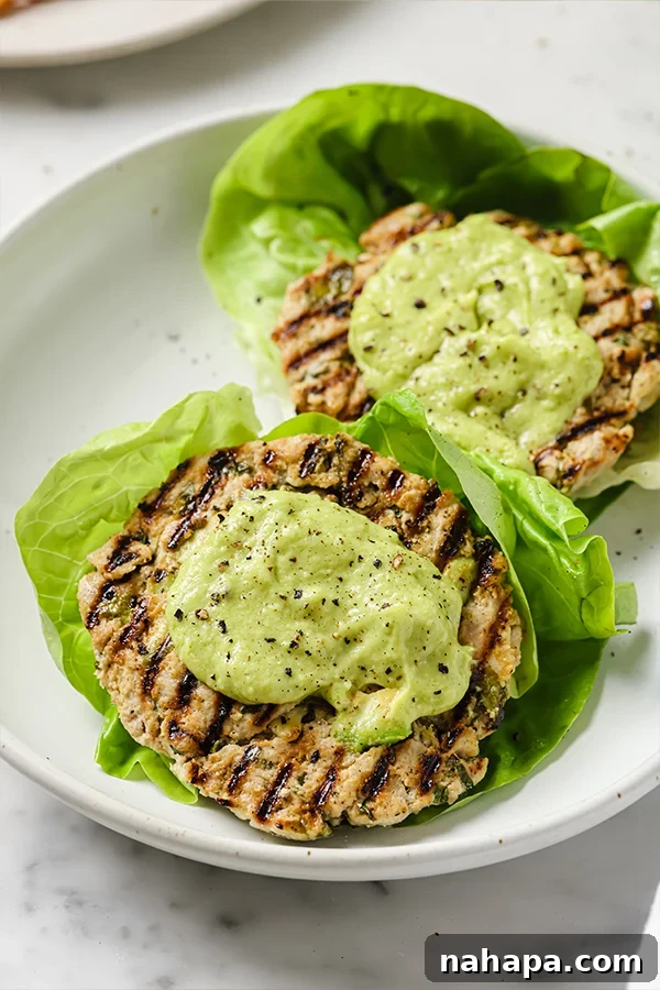 Stacked Spinach Avocado Chicken Burgers on a plate with avocado and cilantro