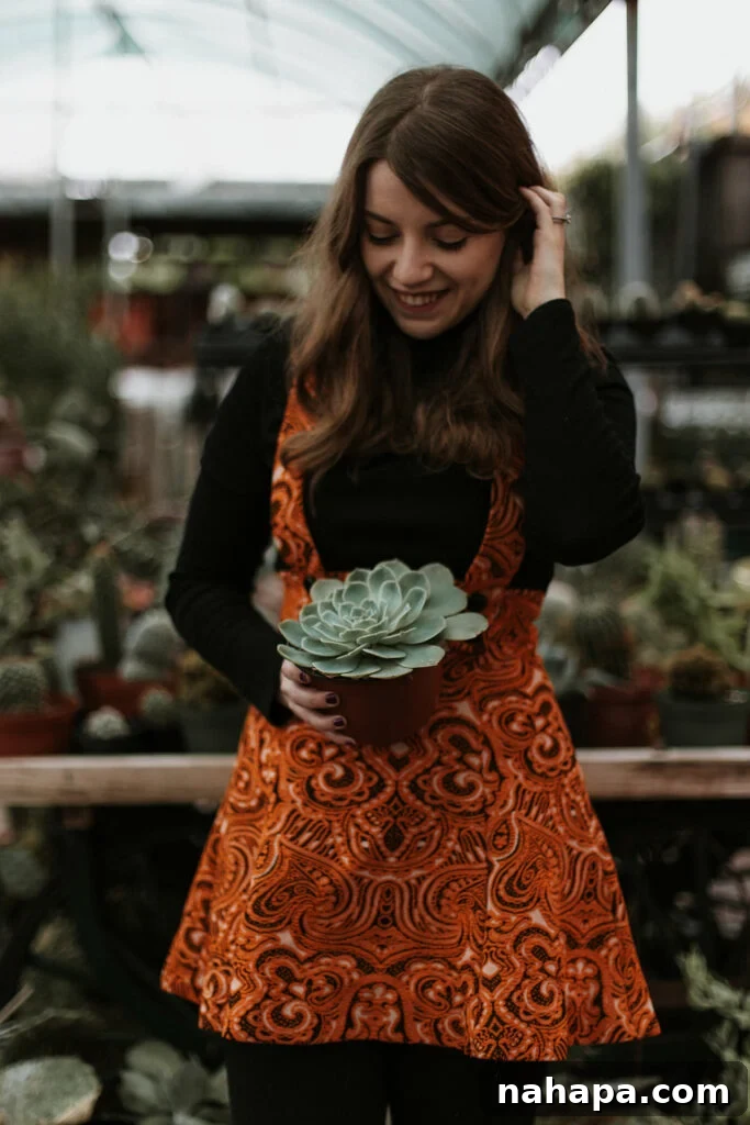 Michelle holding a succulent plant dressed in a black long sleeve top and orange dress.