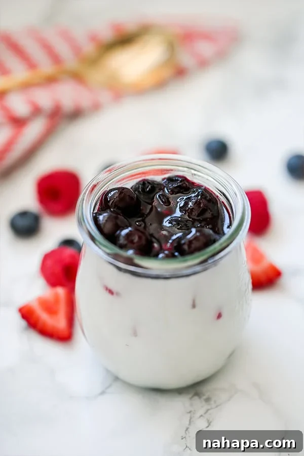 A glass jar filled with red white and blue panna cotta with fresh berries on the counter beside it.