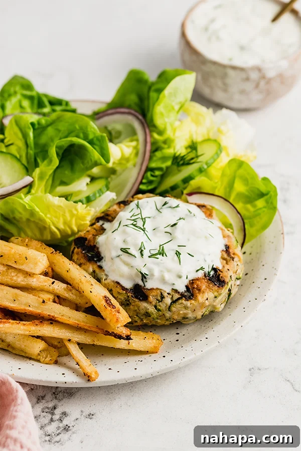 Grilled Greek chicken burger on a plate with greens and fries, highlighting the vibrant colors and fresh ingredients
