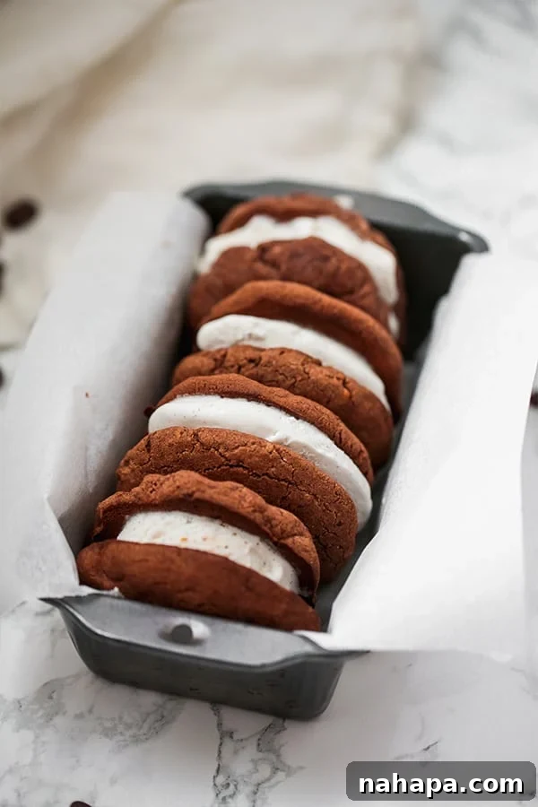 A trio of delicious chocolate cookie ice cream sandwiches nestled in a loaf pan lined with parchment paper, ready to be enjoyed.