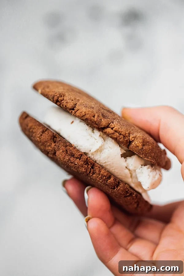 A hand gently holding a freshly made chocolate cookie ice cream sandwich, highlighting its inviting texture.