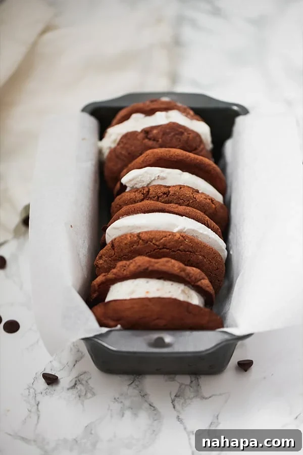 Three perfectly assembled chocolate cookie ice cream sandwiches resting in a parchment-lined loaf pan, waiting to be savored.