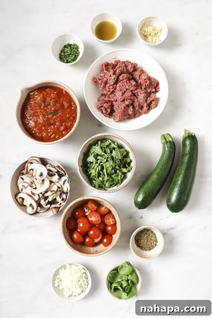 A vibrant display of fresh ingredients for a healthy lasagna skillet, including mushrooms, fresh spinach, and zucchini, ready for preparation.