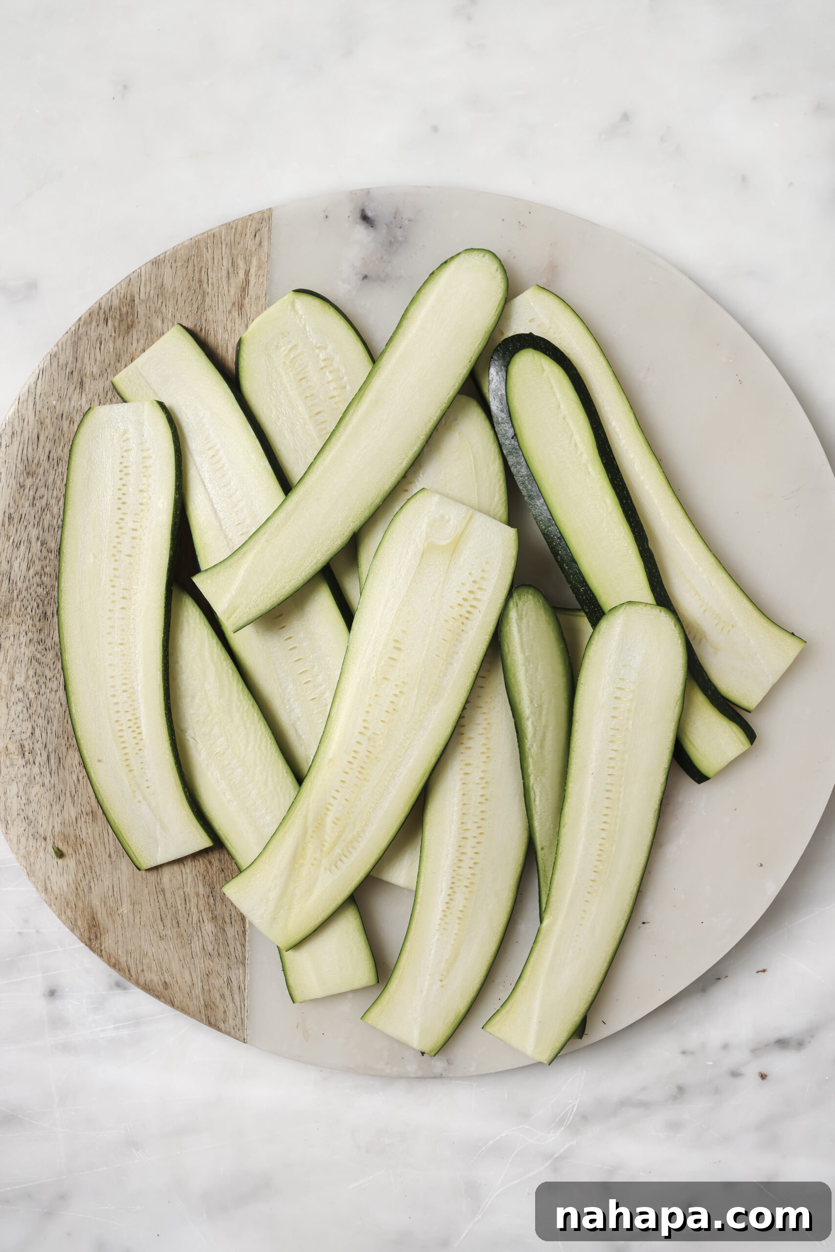 Thin zucchini strips expertly arranged on a round wooden board, showcasing their readiness to become healthy lasagna 'noodles'.