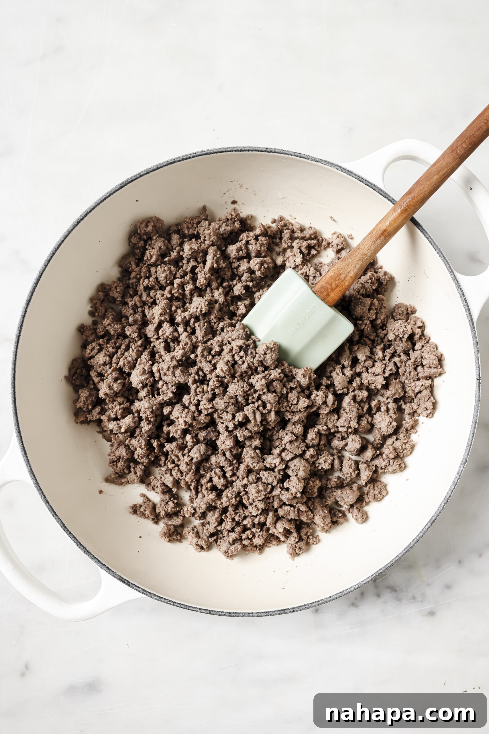 A spatula gently stirs savory browned ground beef in a skillet, ready to be incorporated into the delicious lasagna.