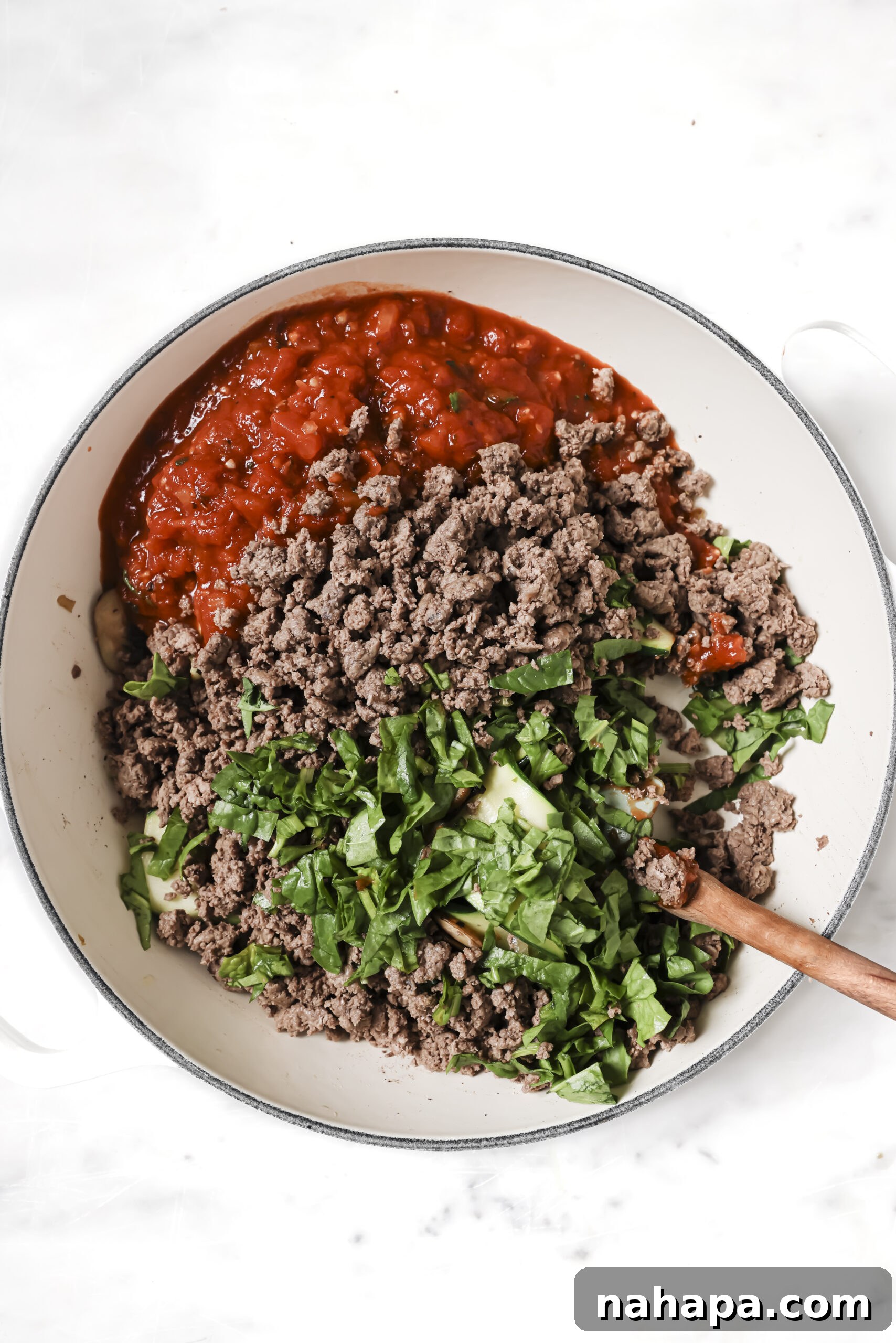 A flavorful combination of marinara sauce, fresh spinach, and browned ground beef simmering together in a pan, creating a rich base for the skillet lasagna.