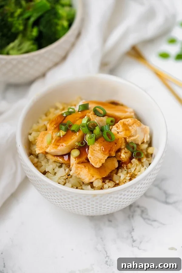 A white bowl with cauliflower rice topped with slow cooker chicken teriyaki and sliced green onion.