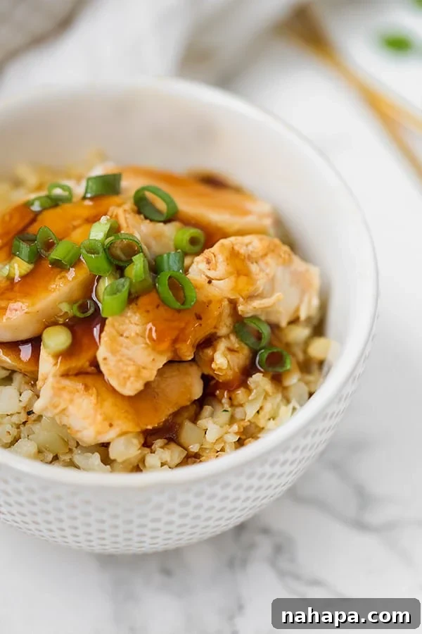 A bowl filled with chicken teriyaki on cauliflower rice topped with sliced green onions.