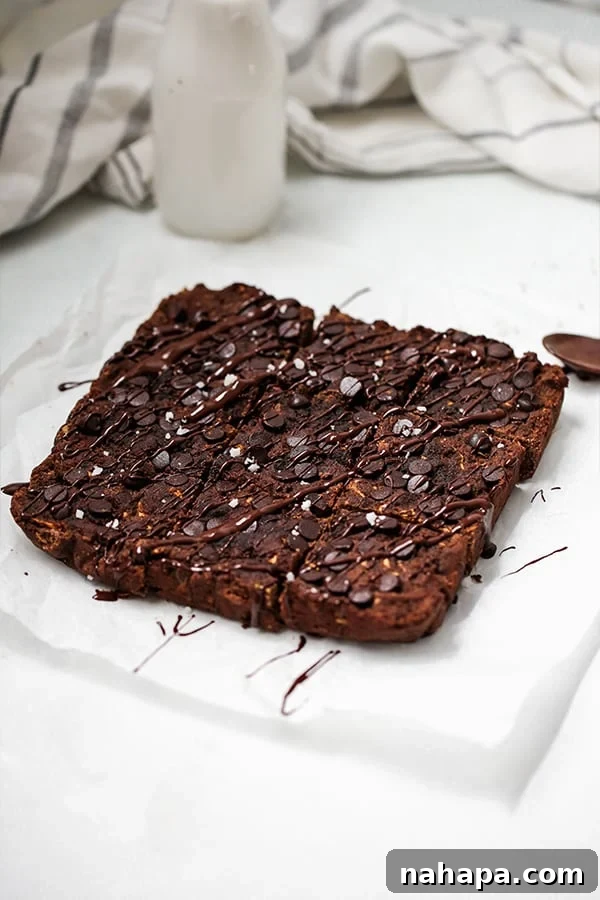 A pan of zucchini brownies cut into squares and sitting on a piece of parchment paper on a countertop.
