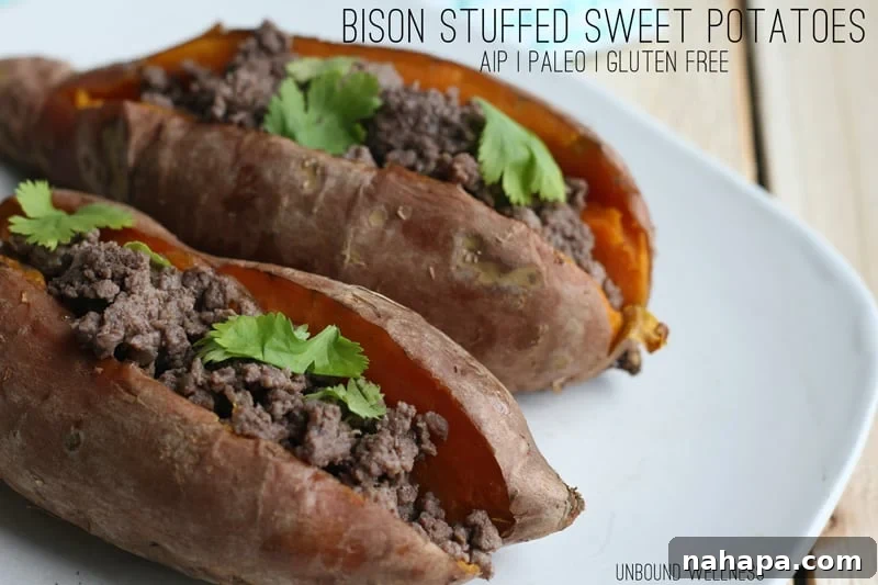 Hearty Bison Sweet Potato Boats 2 Two halves of a delicious bison stuffed sweet potato garnished with fresh cilantro on a white plate with a fork.