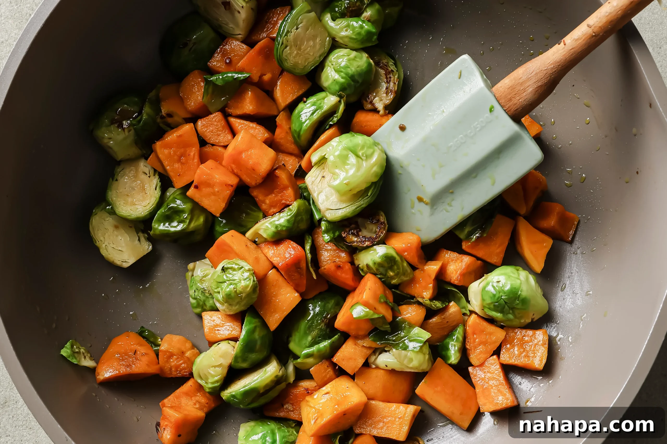 Diced sweet potatoes and halved Brussels sprouts sautéing in a pan with avocado oil.