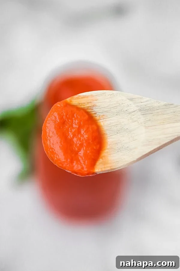 A wooden spoon taking a little bit of nightshade free marinara sauce out of the glass bottle of it.