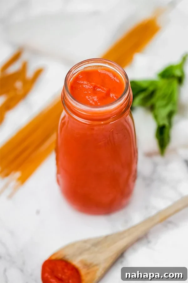 A glass jar filled with nightshade free marinara sauce with pieces of uncooked spaghetti lying next to it.