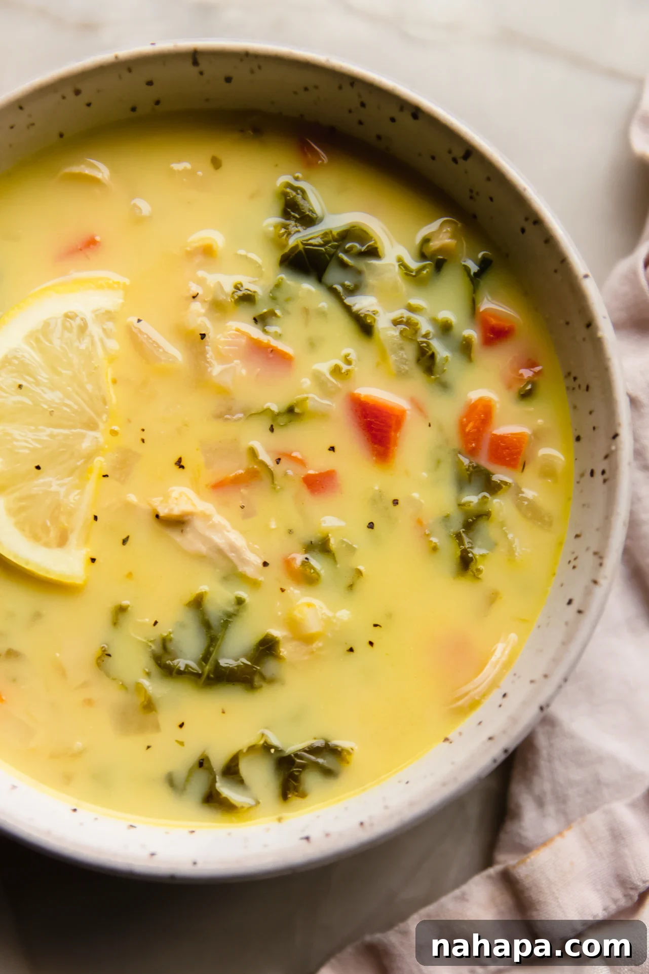 Velvety Greek Lemon Chicken Avgolemono 2 A comforting bowl of Greek lemon chicken soup, garnished with a fresh lemon wedge and herbs.
