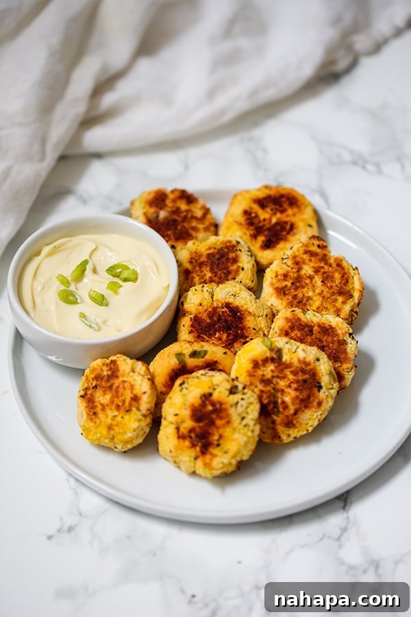 Close-up of crispy, golden-brown spaghetti squash nuggets piled on a plate, garnished with fresh green herbs.