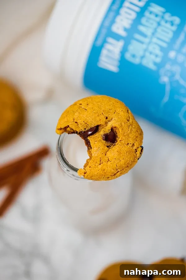 Nourishing Paleo Pumpkin Chocolate Chip Cookies 5 A pumpkin chocolate chip cookie balanced on the top of a glass with a bite taken out of the cookie.