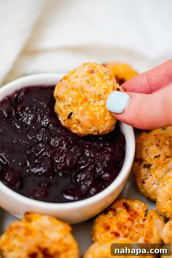 Flavorful Butternut Chicken Poppers Paleo Whole30 AIP 3 A hand dipping a butternut chicken popper into a vibrant red cranberry sauce.