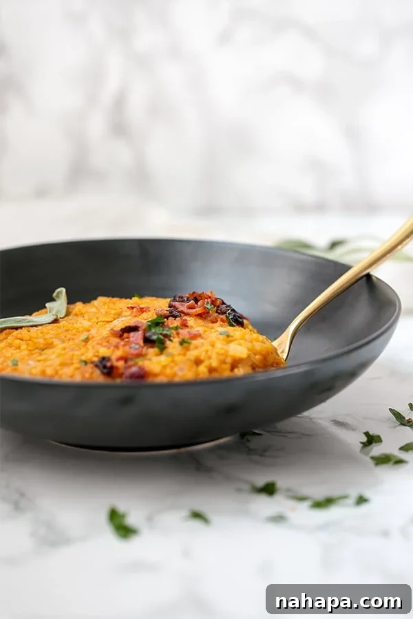 Creamy Paleo Whole30 AIP Cauliflower Pumpkin Risotto 3 A close-up shot of creamy pumpkin risotto in a black bowl, with a metal spoon, showcasing the rich texture and garnishes.
