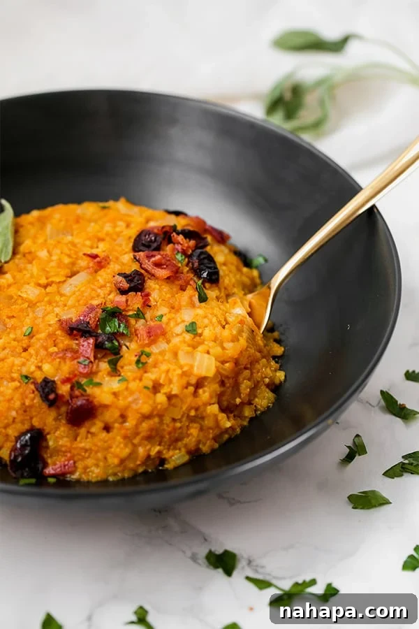 A black bowl filled with creamy cauliflower pumpkin risotto, garnished with fresh herbs and a spoon resting in it.