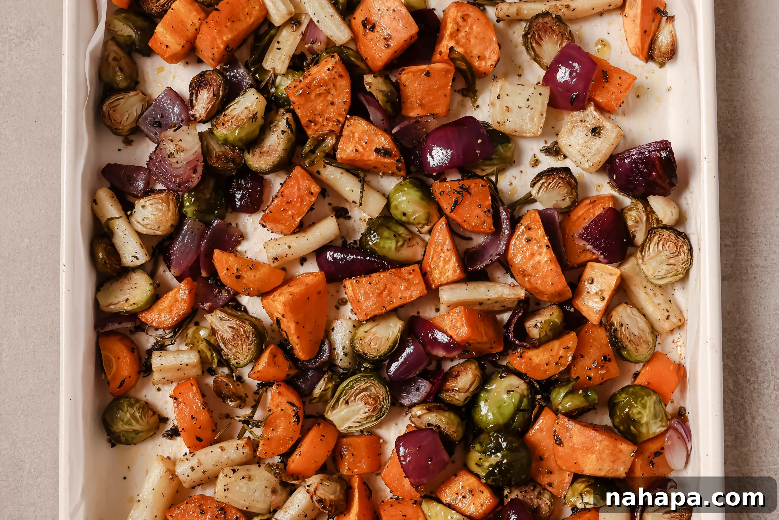 Bountiful Harvest Veggie Hash 7 Roasted vegetables, including sweet potato, parsnip, Brussels sprouts, and red onion, looking golden and slightly charred on a baking sheet.