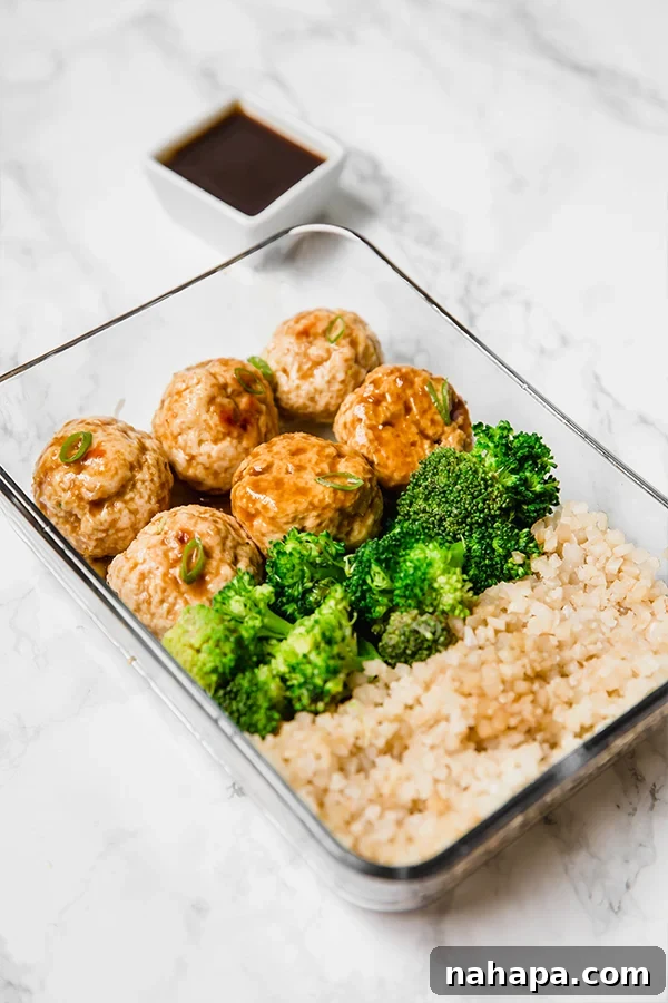 A glass meal prep container filled with vibrant teriyaki chicken meatballs, crisp green broccoli florets, and fluffy white cauliflower rice, ready for a healthy and convenient meal.