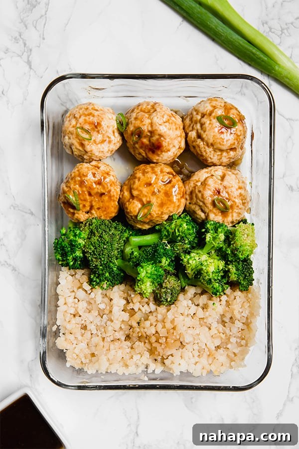 A top-down view of an open glass meal prep container filled with golden-brown teriyaki chicken meatballs, bright green steamed broccoli, and fluffy cauliflower rice.