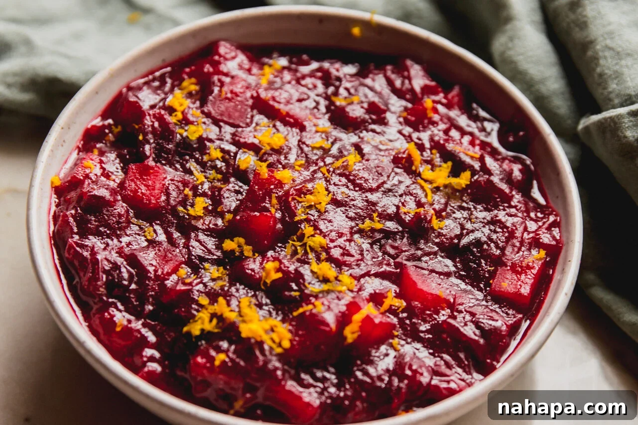 Spiced Apple Cranberry Compote 7 A serving of apple cranberry sauce in a white bowl, garnished generously with fresh orange zest on top.