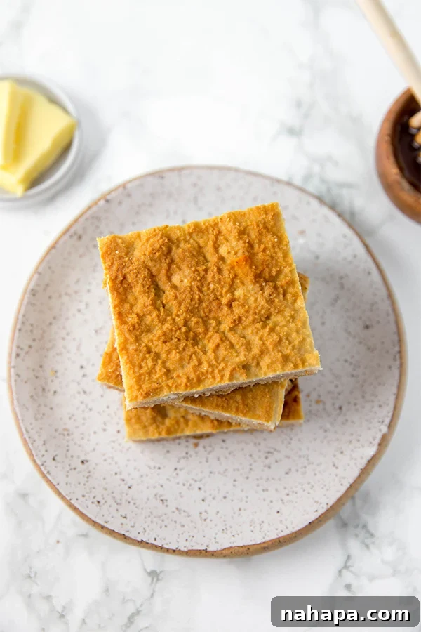 A stack of golden brown grain-free cornbread squares on a rustic grey plate, with a knife and butter nearby.