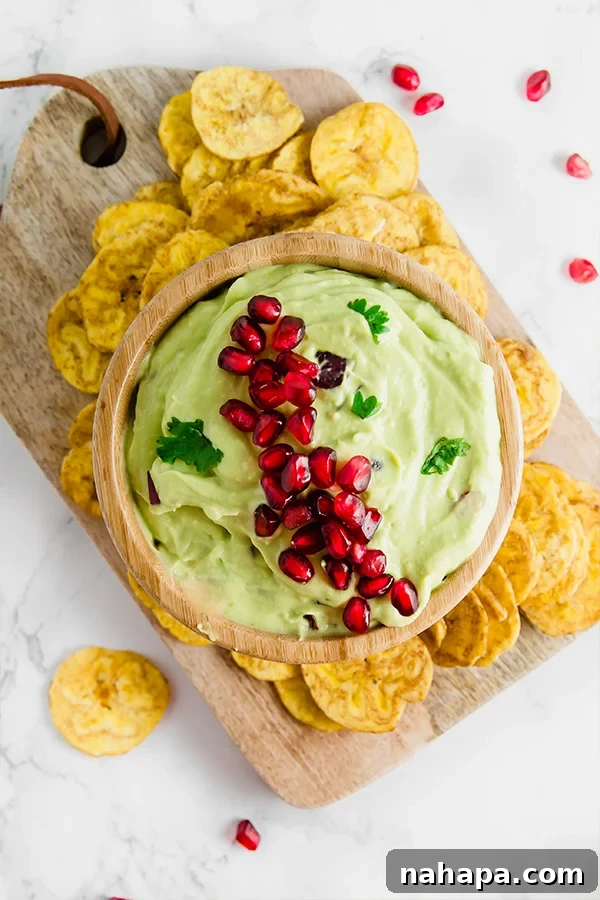 Tangy Pomegranate Guacamole Paleo AIP Vegan Approved 4 Pomegranate guacamole in a wooden bowl with plantain chips, ready to be served as a healthy, festive appetizer.