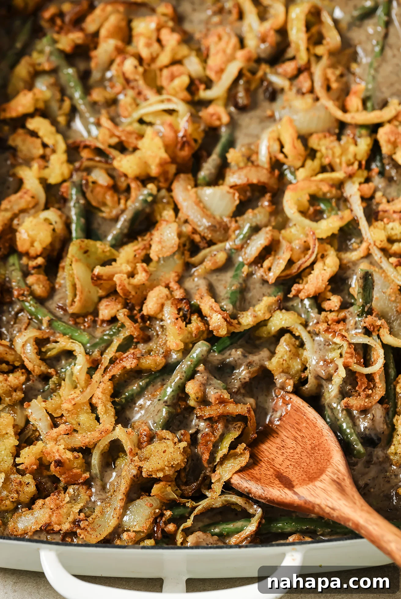 Green bean casserole and fried onions in a casserole dish with a spoon dipping in.