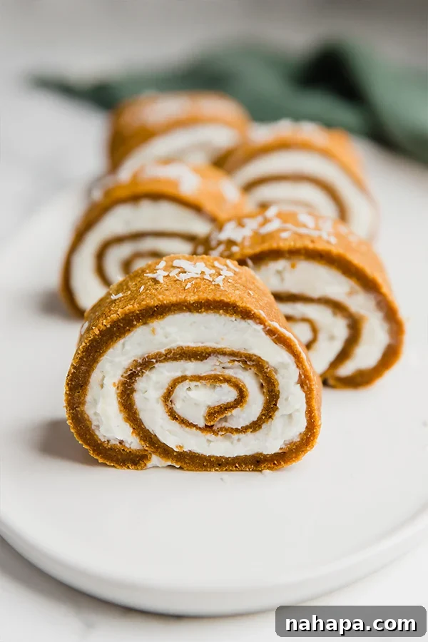 A beautifully spiraled paleo pumpkin roll cake, dusted with powdered sugar, sitting on a wooden cutting board.