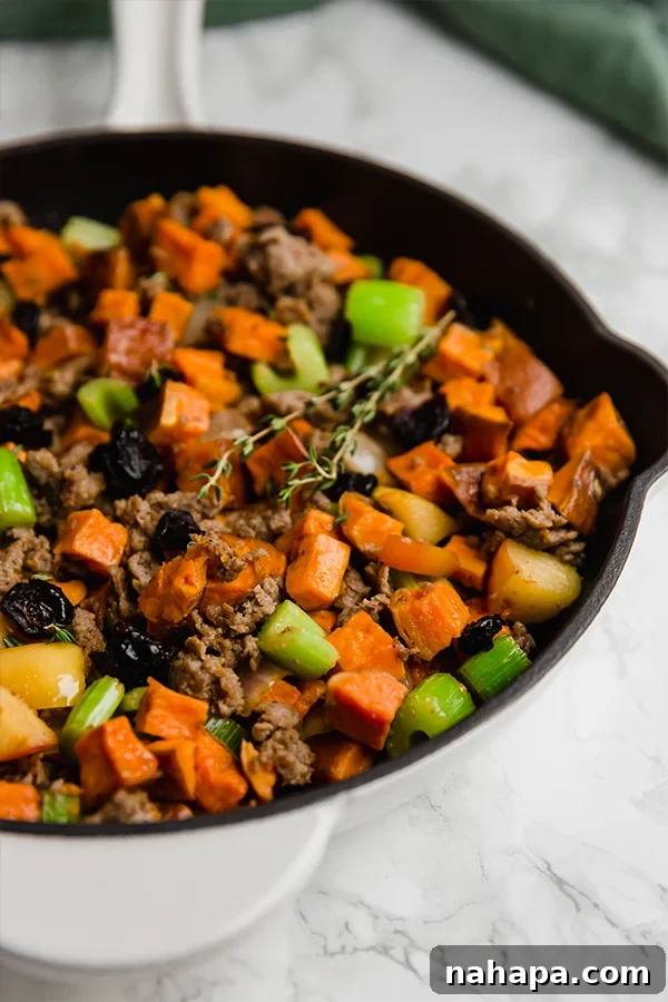 A rustic cast iron skillet filled with savory sweet potato sausage stuffing, garnished with fresh herbs, ready for the Thanksgiving table.