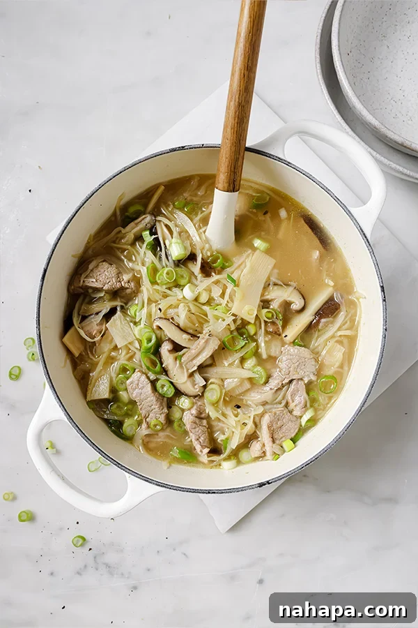 A steaming pot of homemade hot and sour soup, garnished with fresh green onions, ready to be served in a rustic bowl.
