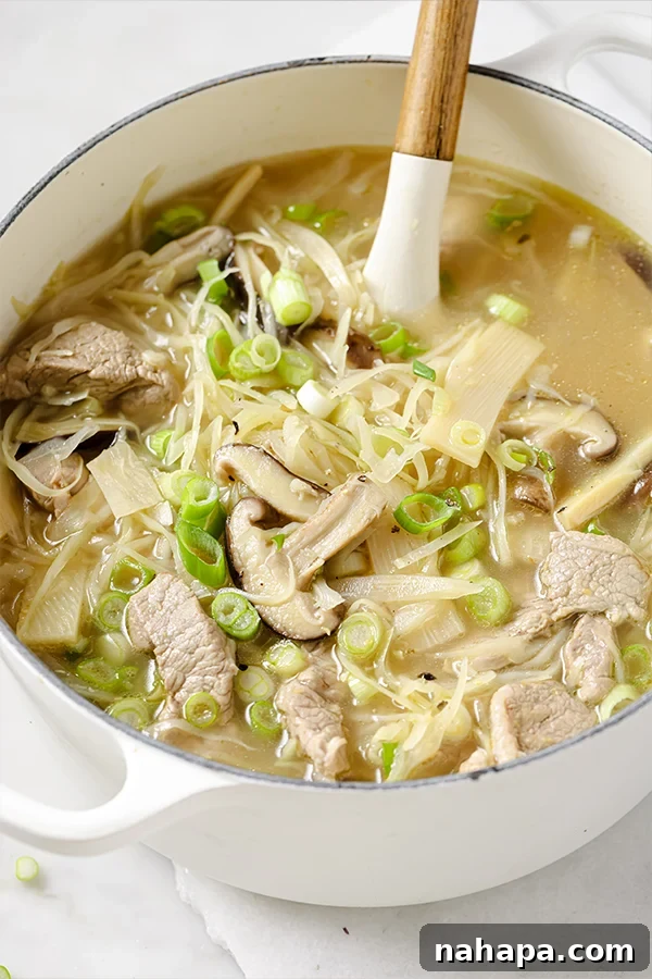 A pot of hot and sour soup with a wooden spoon stirring the rich, dark broth, showcasing the various ingredients like mushrooms and pork.