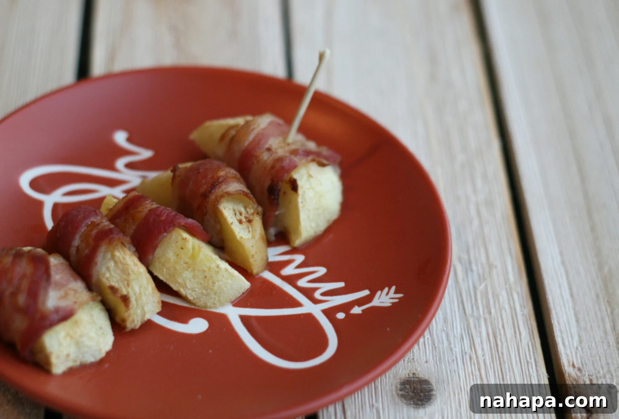 Pumpkin spice baked apple slices wrapped in bacon on an orange plate.