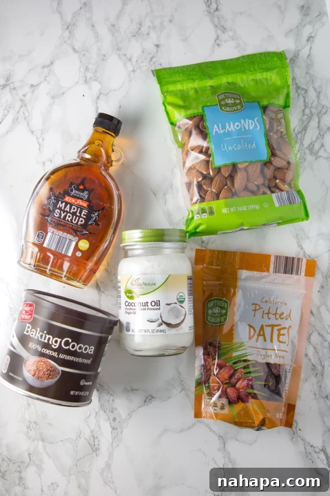 An array of five key ingredients for healthy no-bake cookies: maple syrup, coconut oil, baking cocoa, whole almonds, and dates, neatly arranged on a kitchen counter.