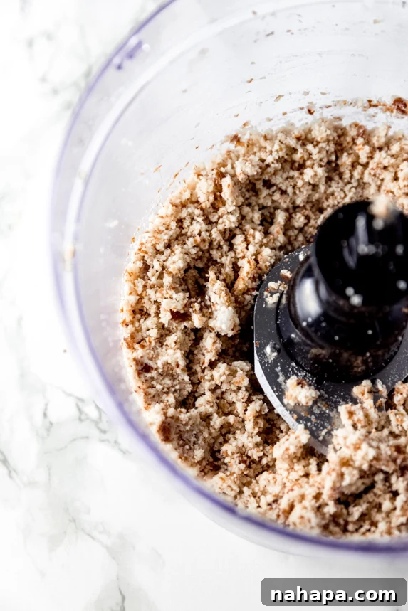 A high-speed food processor actively grinding whole nuts and dates, transforming them into a smooth, consistent dough for no-bake cookies.