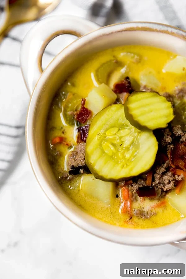 A pristine white bowl generously filled with savory bacon cheeseburger soup, beautifully topped with extra pickles, inviting you to enjoy.