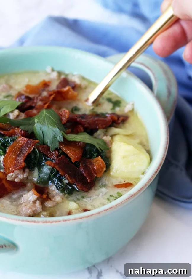 A vibrant blue bowl of Paleo & AIP Zuppa Toscana, sumptuously topped with crispy, savory bacon bits.